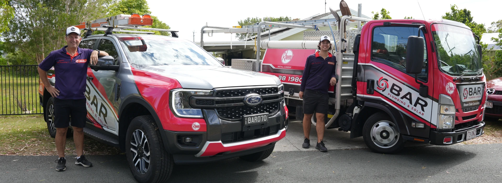 Bar Plumbing team standing beside two Bar Plumbing trucks